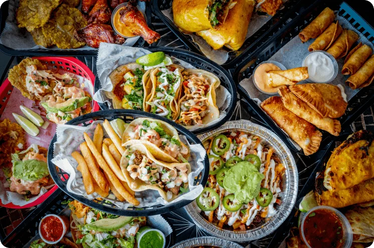 A catered spread of tacos, loaded fries, burritos, plantains, and sides